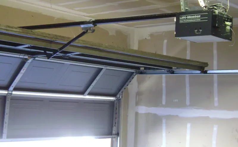 Garage door opener rail and motor mounted above a sectional door, with the spring hardware visible